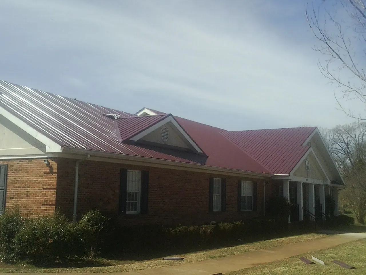 Red metal roof with gabled entries on a long brick building, from a Hail Damage Roof Repair job in Taneytown