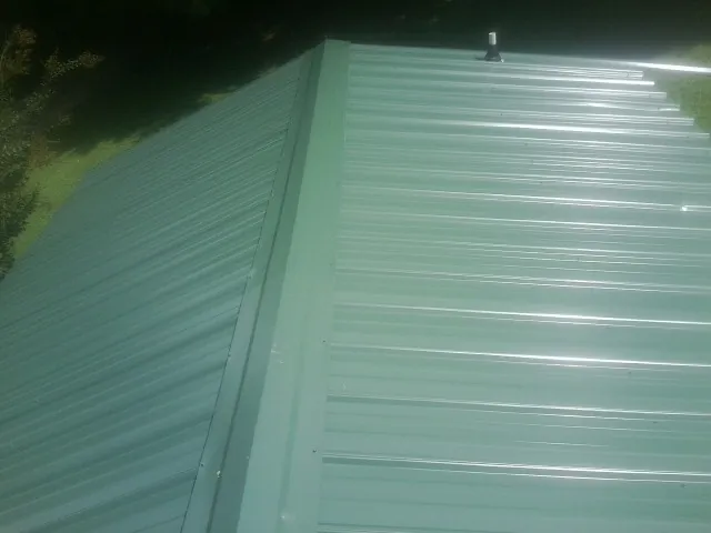 New green metal panels meeting at the ridge of a roof — Flat Roof Repair work by our crew in Taneytown