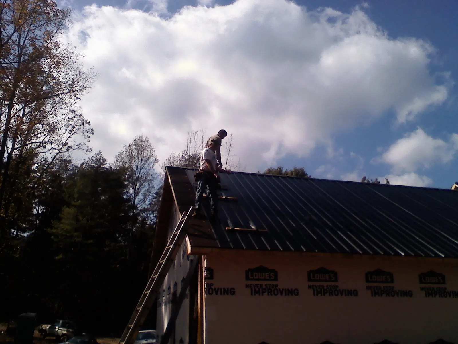 Roofer fastening dark metal panels high against a cloudy sky, from a Roof Inspection job in Taneytown