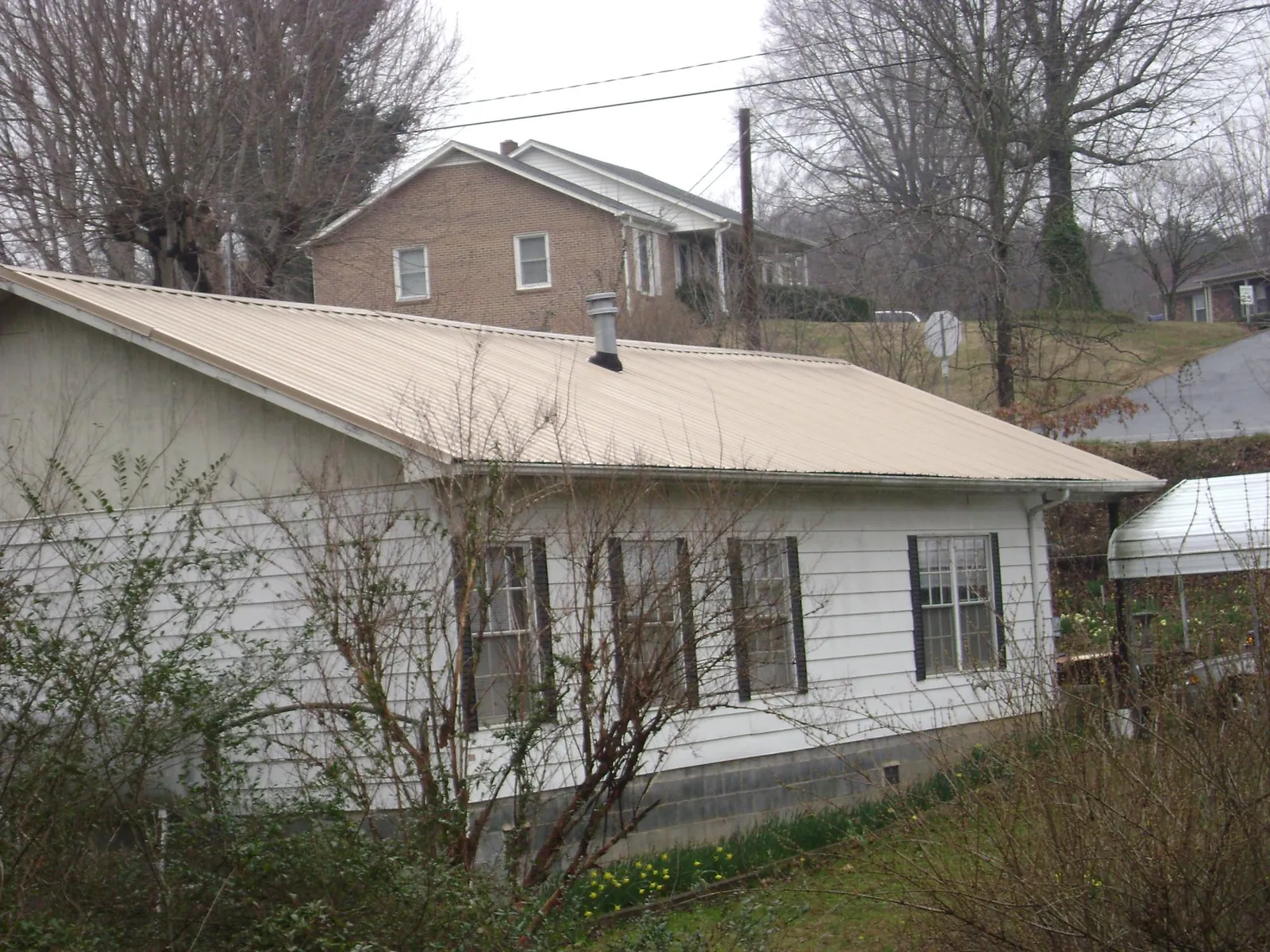 Tan metal roof on a white sided house set into a hillside — Commercial Roofing by Roofing Brothers in Taneytown